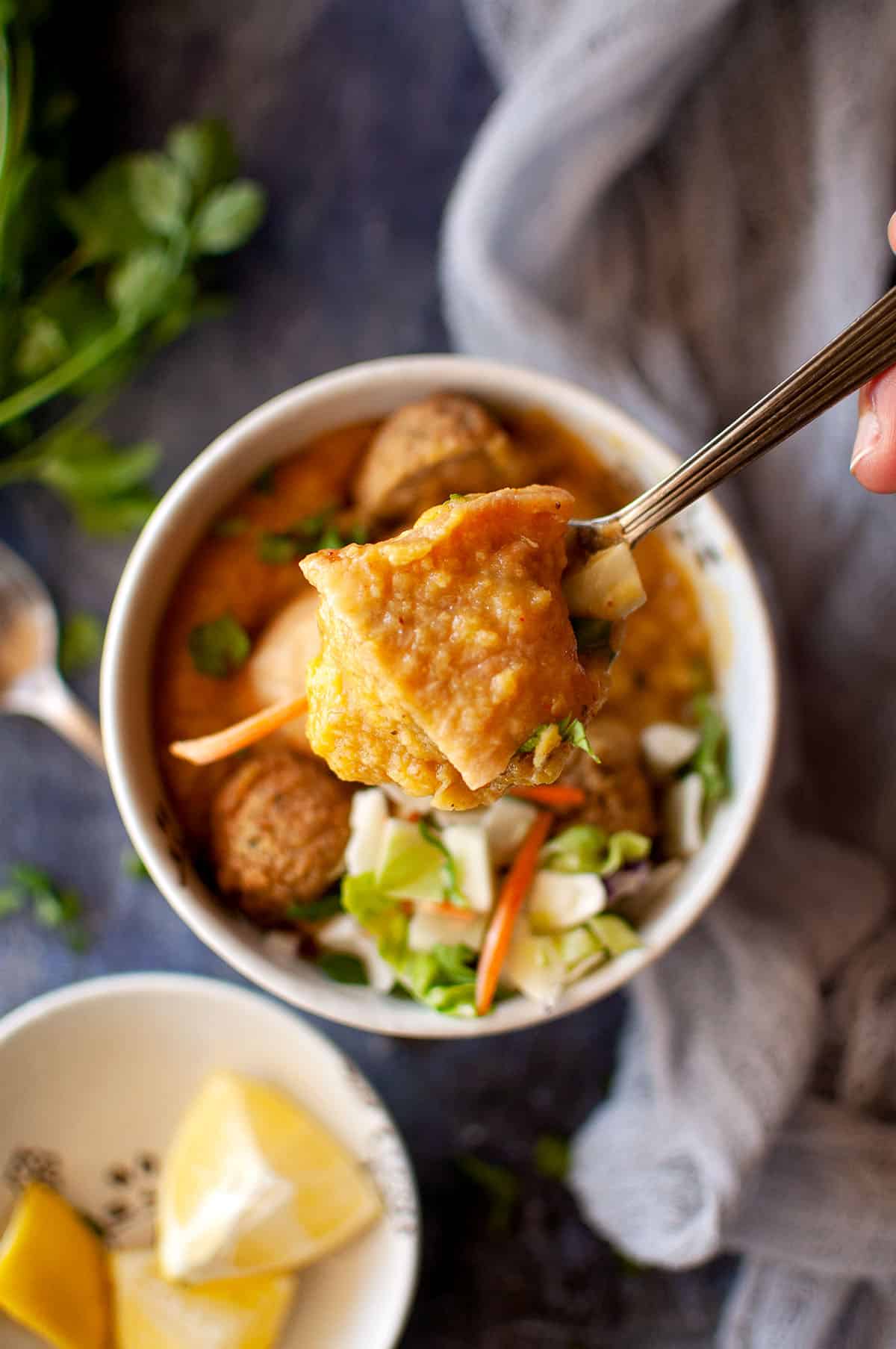 Spoon holding a samosa piece over a bowl of soup.