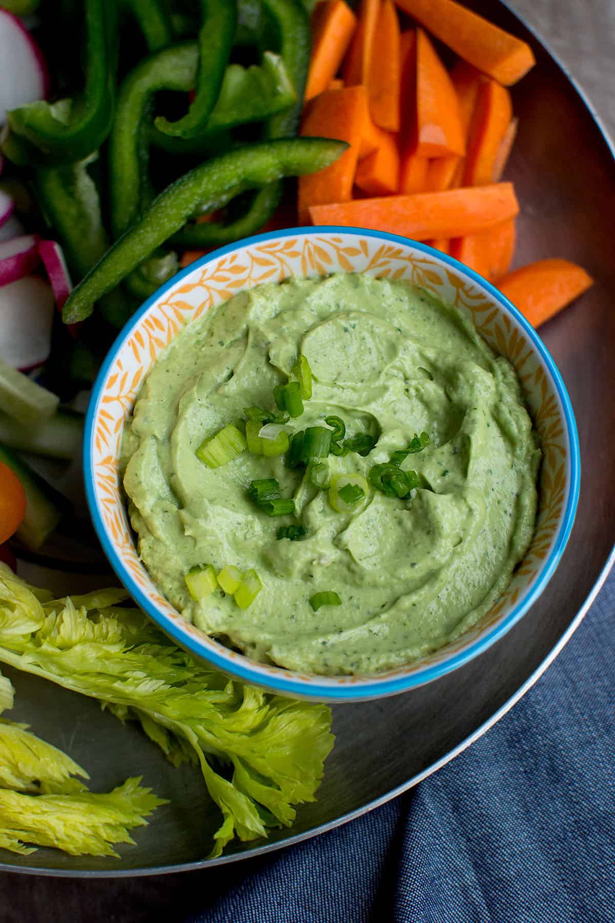 Pewter tray with a white bowl of avocado green goddess dip.
