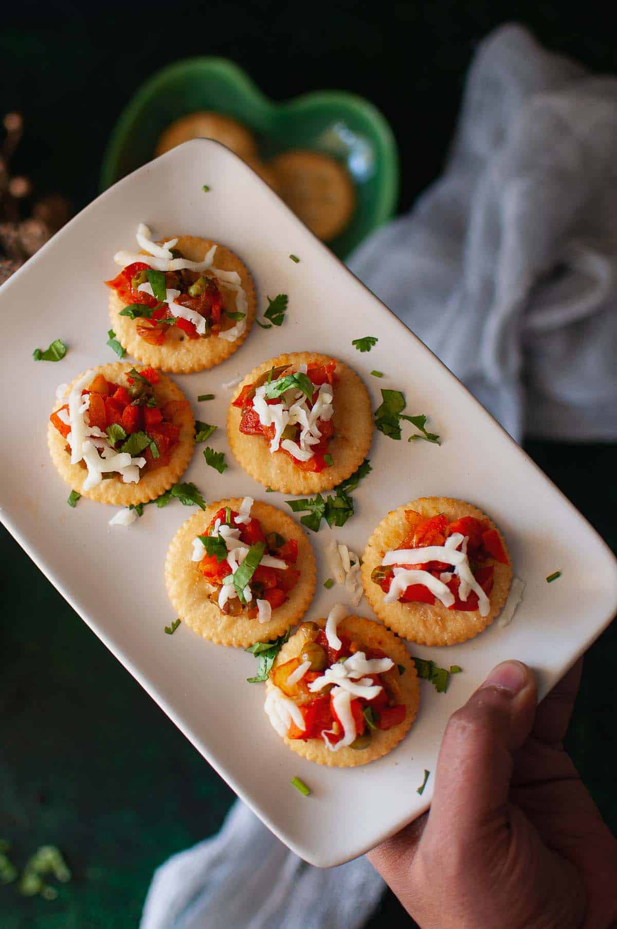 Hand holding a white plate with veg canapes