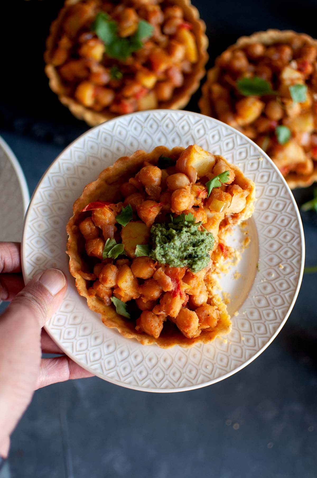 Hand holding a plate of Chana chaat tart topped with green chutney