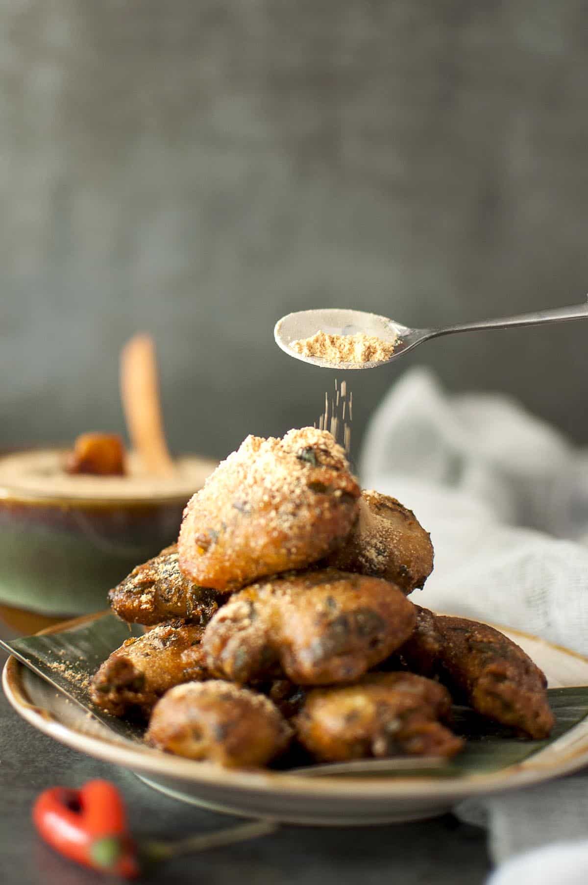 spoon sprinkling spice powder on a stack of palakura punukulu