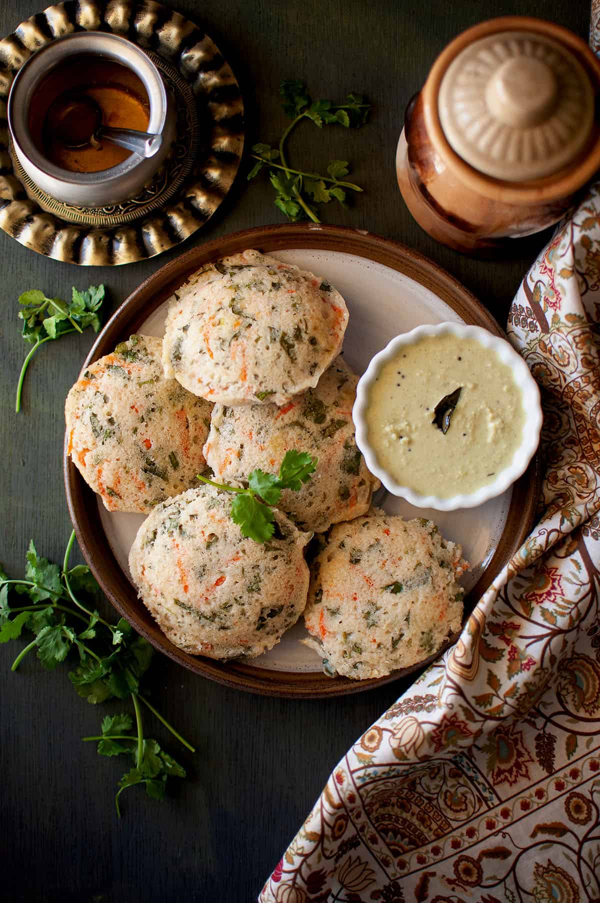 Brown plate with vegetable idli and a white bowl of chutney.