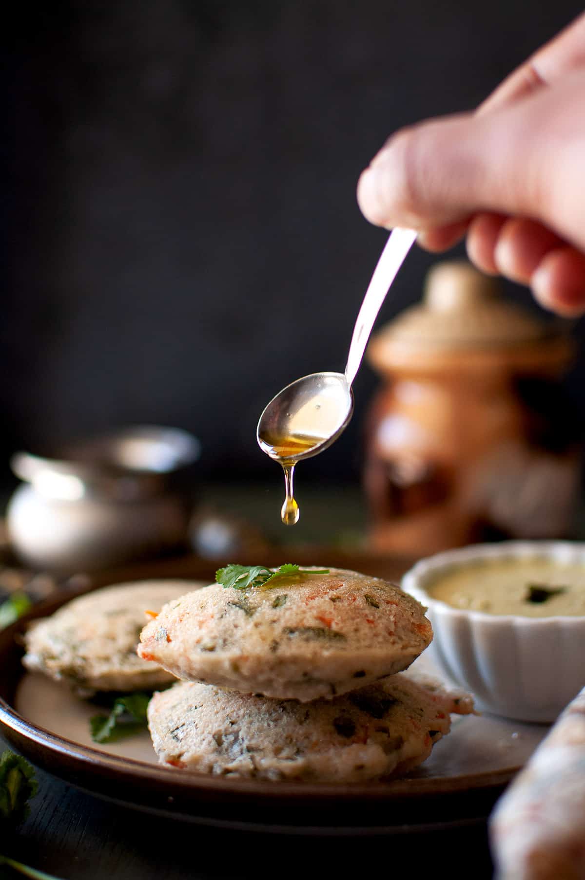 Hand drizzling ghee on a stack of idli.