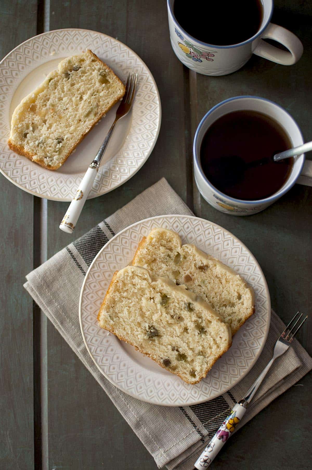 Two slices of Ice Cream bread on a white plate with mugs of tea in the background