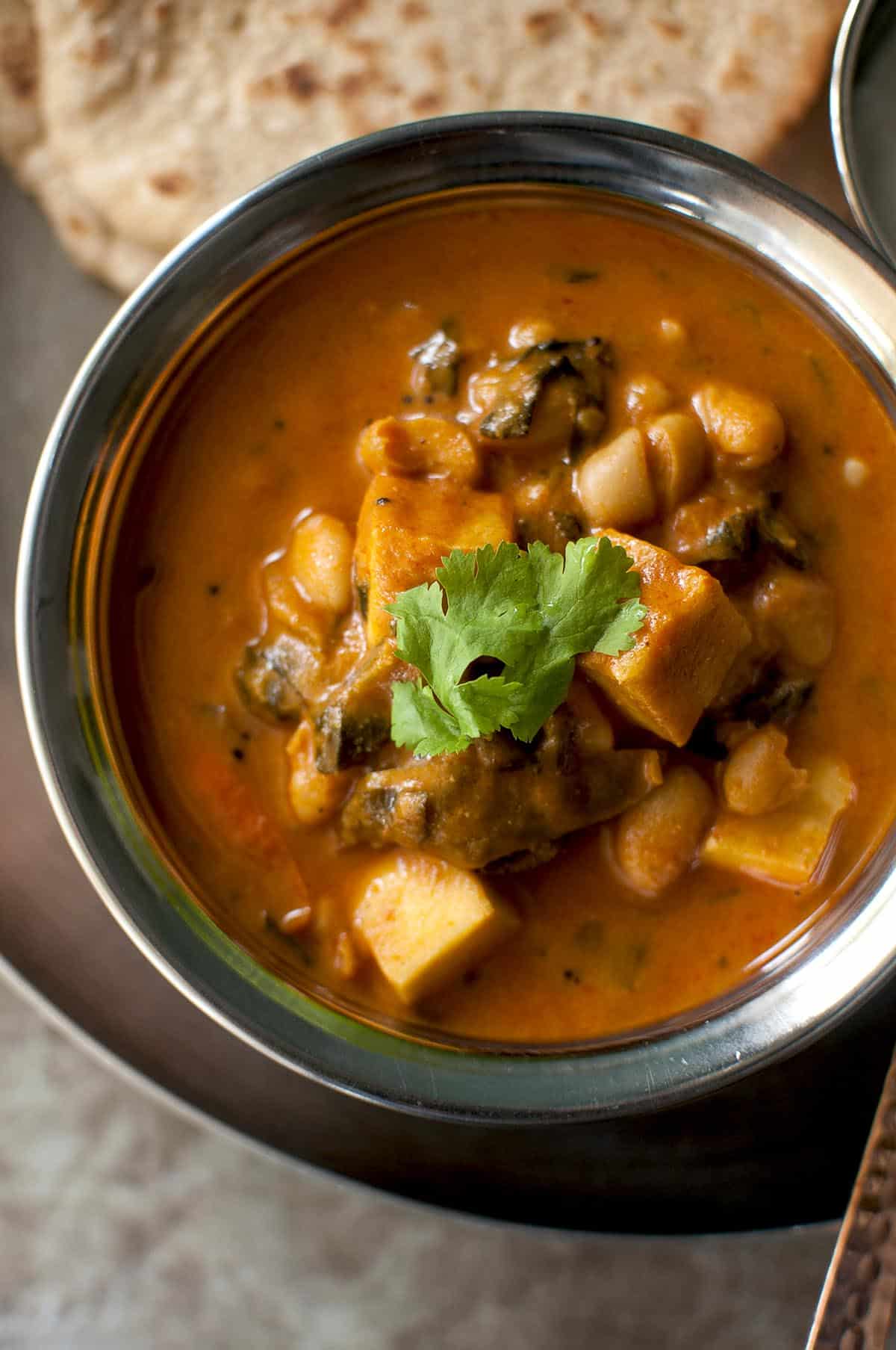 Top view of a steel bowl with paneer and white bean curry