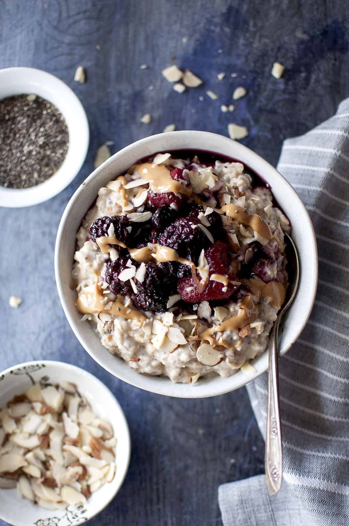 Grey bowl with oat and chia porridge topped with chopped nuts, berries and peanut butter