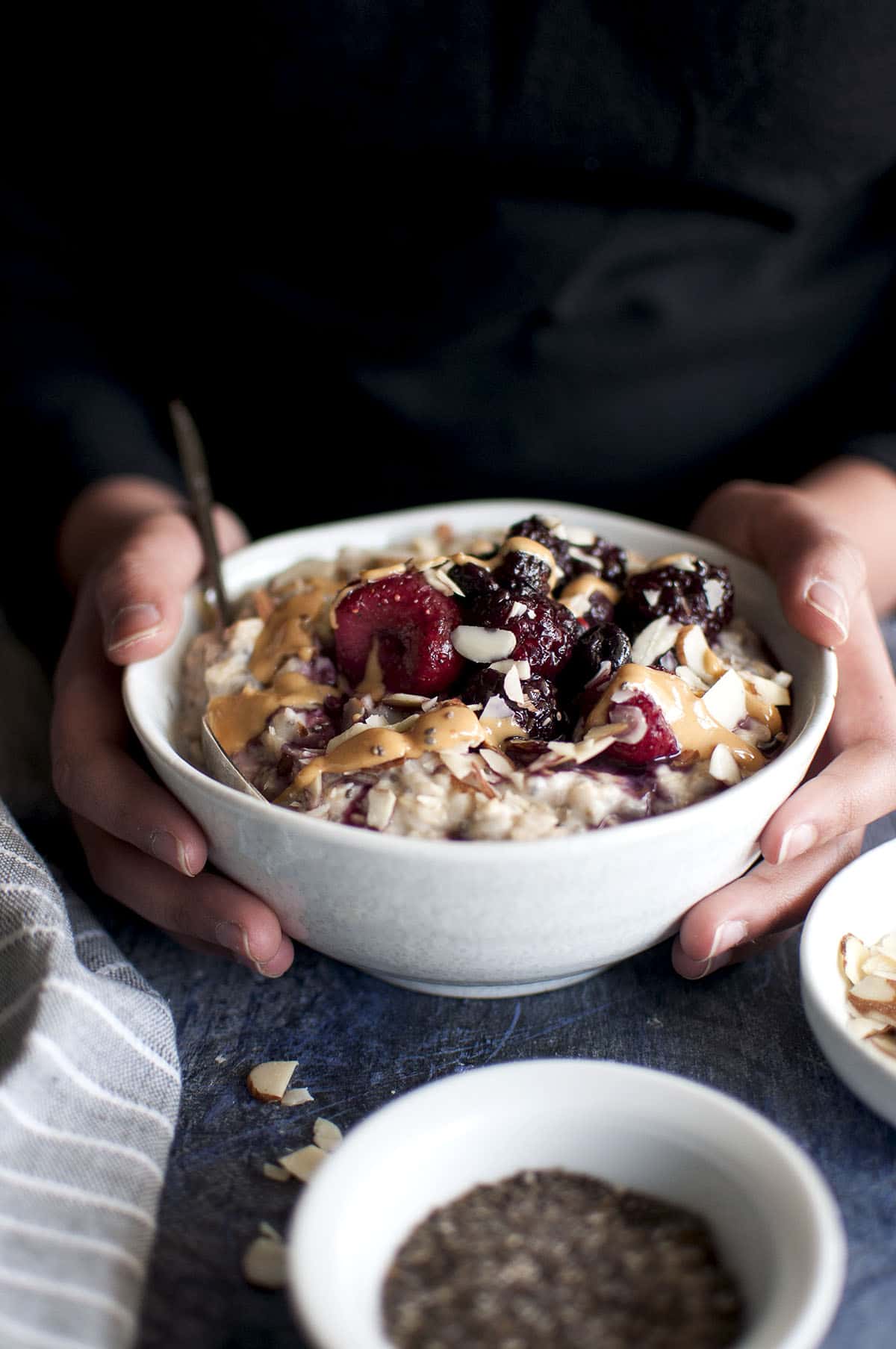 Hand holding a bowl of oatmeal porridge topped with berries.