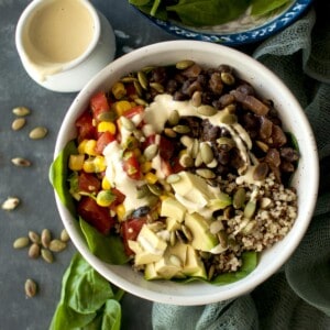 Top view of a white bowl with quinoa, beans, salsa and sauce