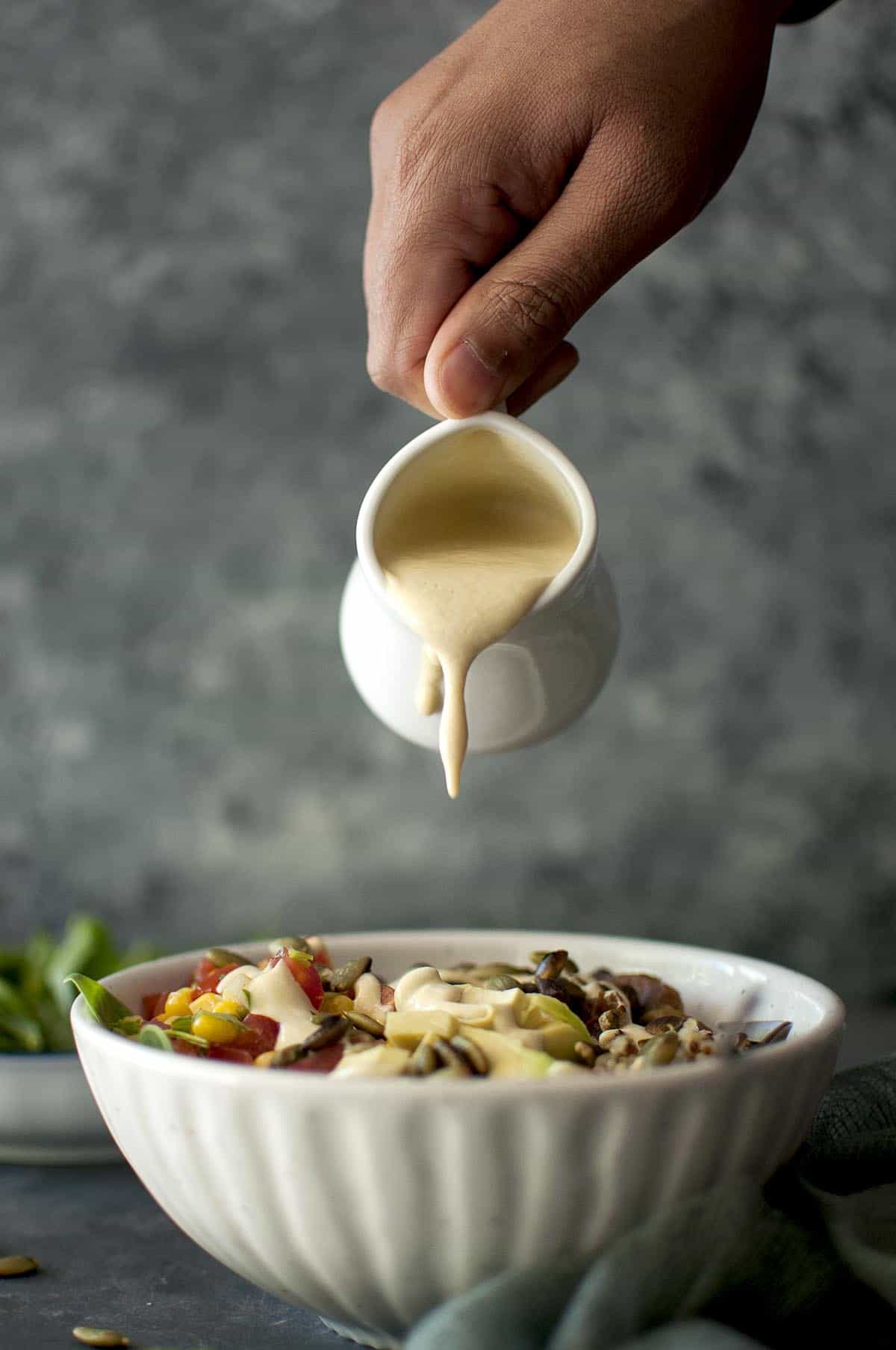 hand pouring cashew queso over Mexican Buddha bowl