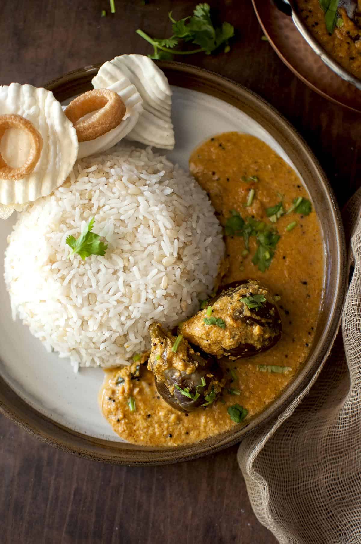 Brown plate with rice, eggplant curry and papad.