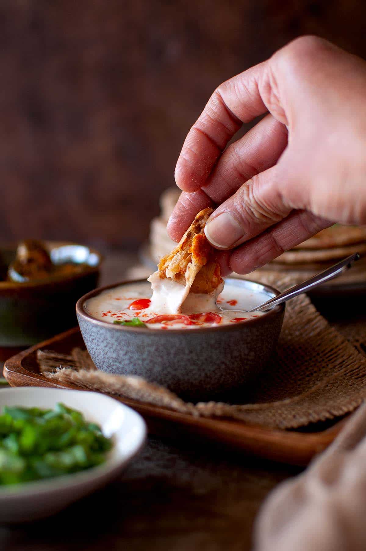 Hand dipping piece of flatbread in raita