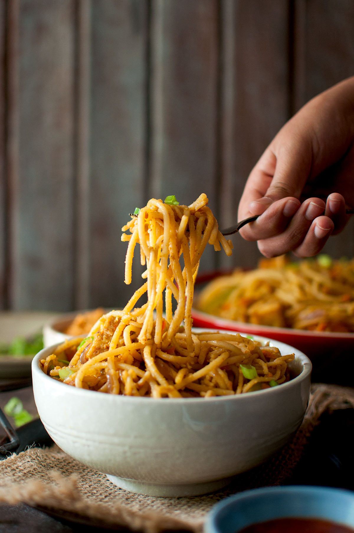 Hand holding spaghetti with fork over a bowl of pasta.