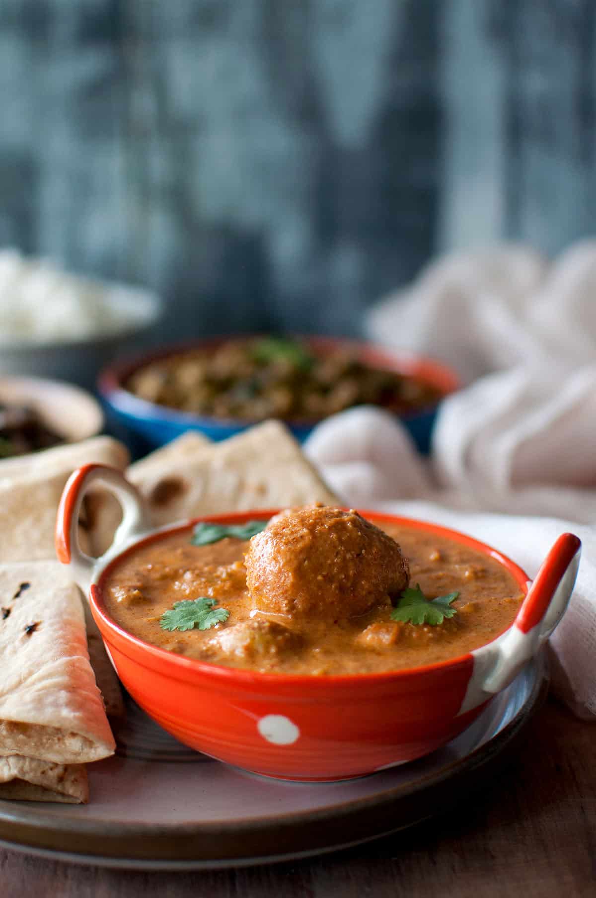 White plate with Orange serving bowl with Lahori Dum Aloo and roti.