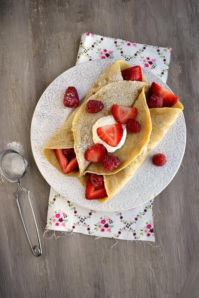 White plate with crepes stuffed with berries and topped with whipped cream