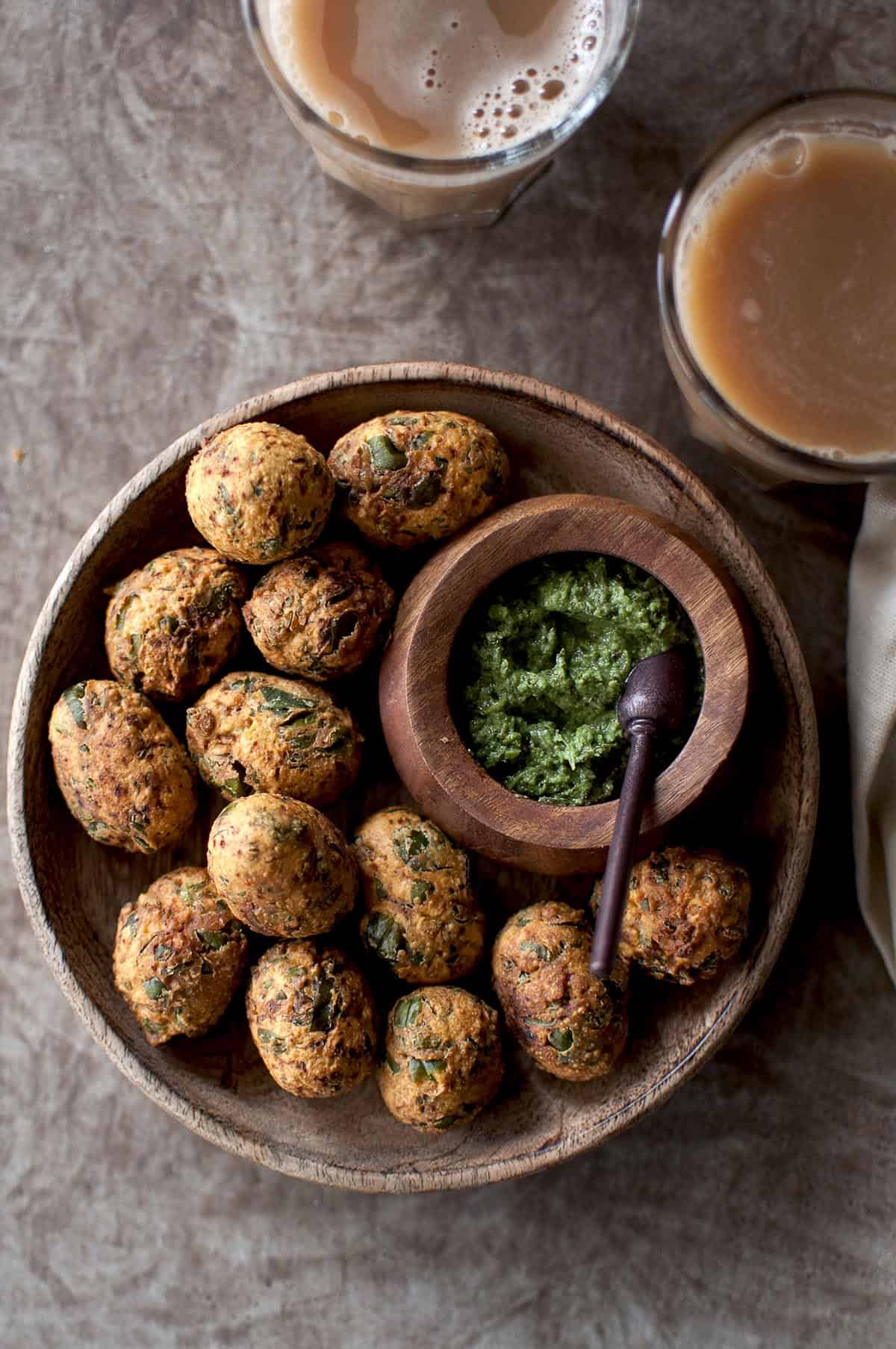 wooden bowl with fried methi muthiya and a bowl of green chutney