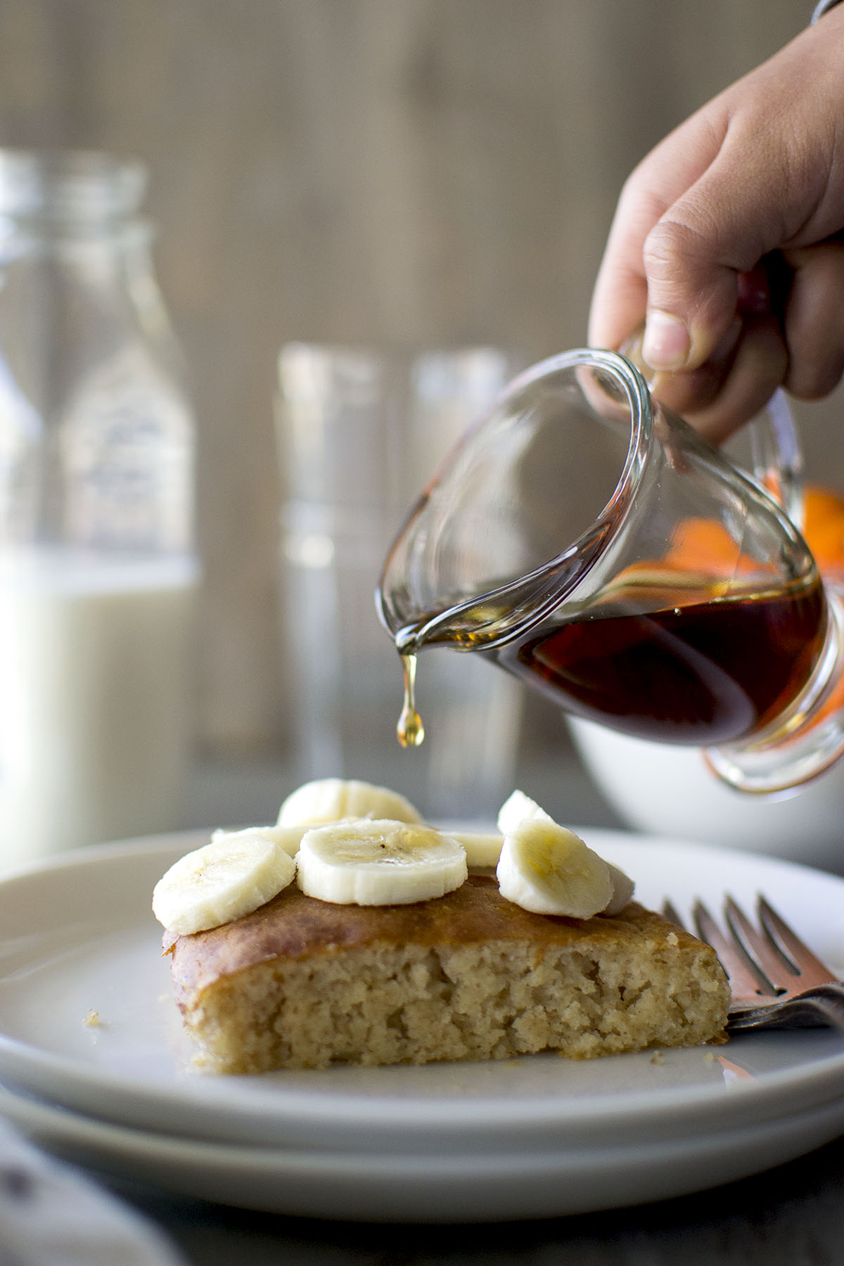 Hand pouring maple syrup onto a bananana topped pancake