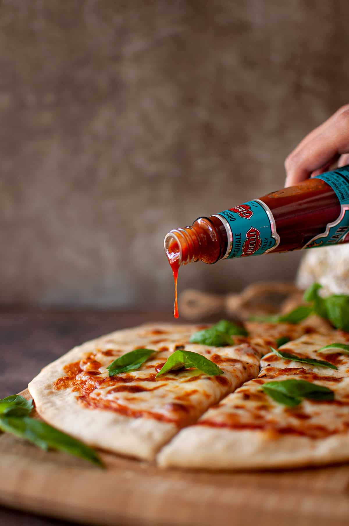 Hand pouring hot sauce from a bottle onto a flatbread.