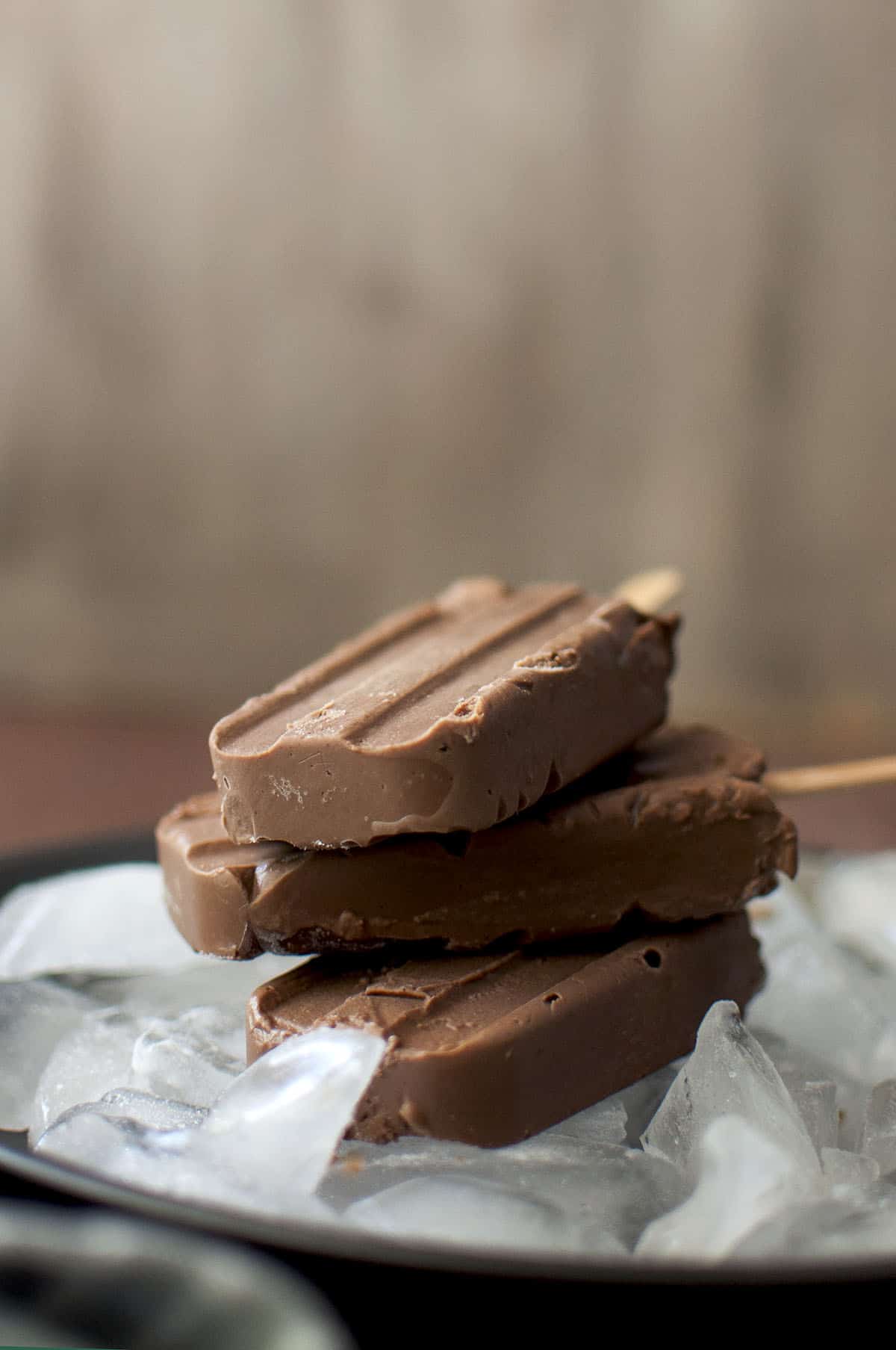 Stack of 3 chocolate popsicles on a tray with ice cubes