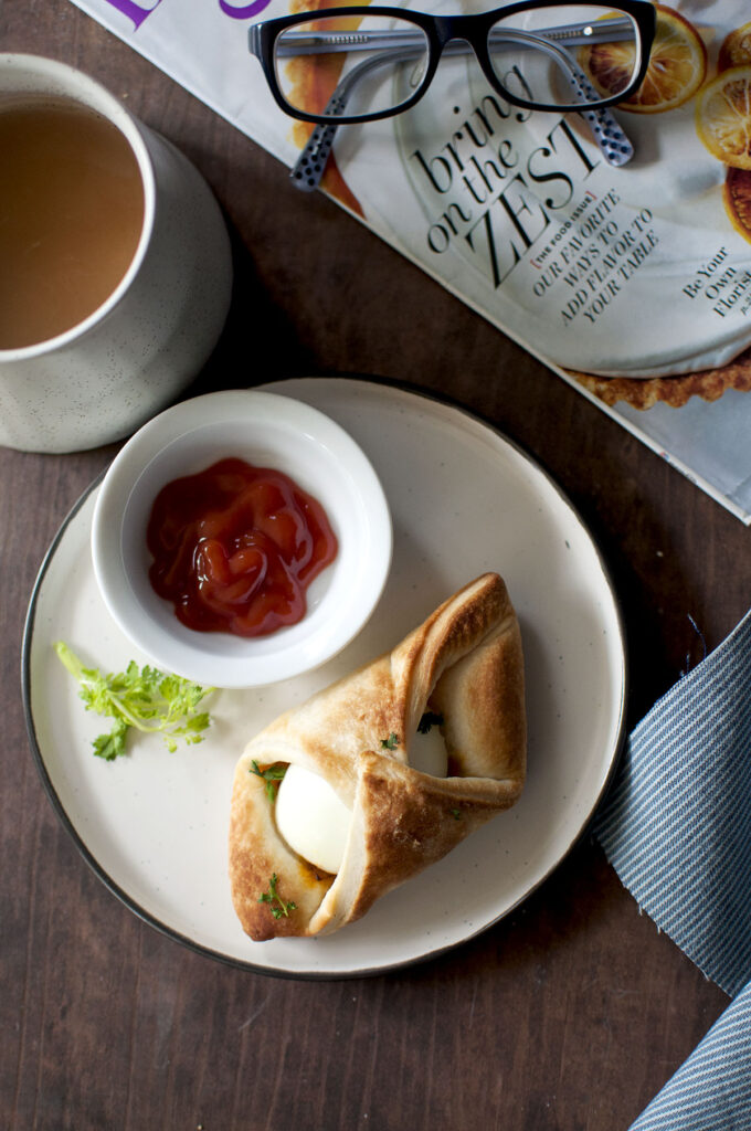 Black plate with egg puff and small bowl with ketchup and a mug of tea