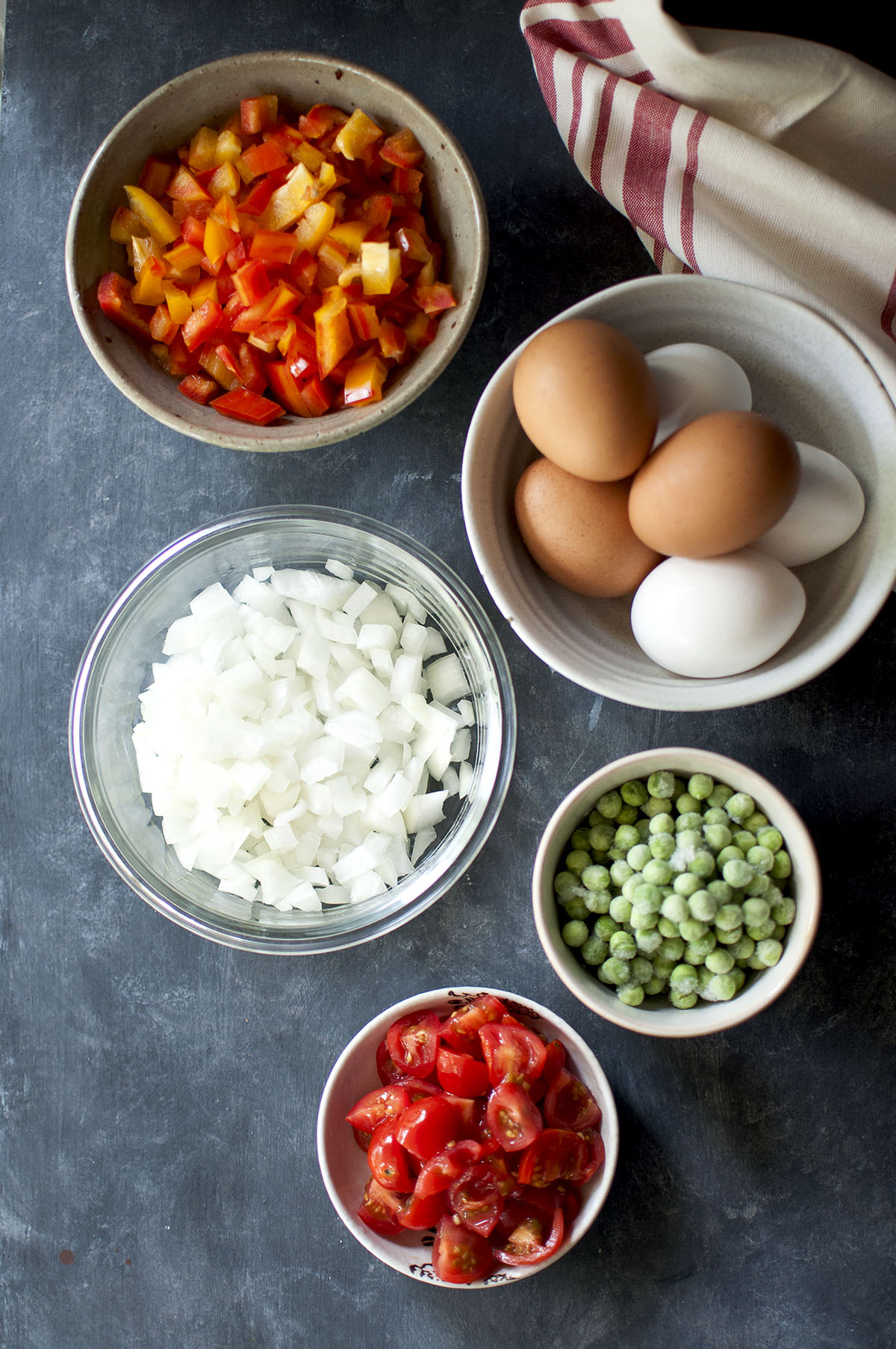 Bowls with chopped bell peppers, onions, tomatoes, frozen peas and bowl of white & brown eggs