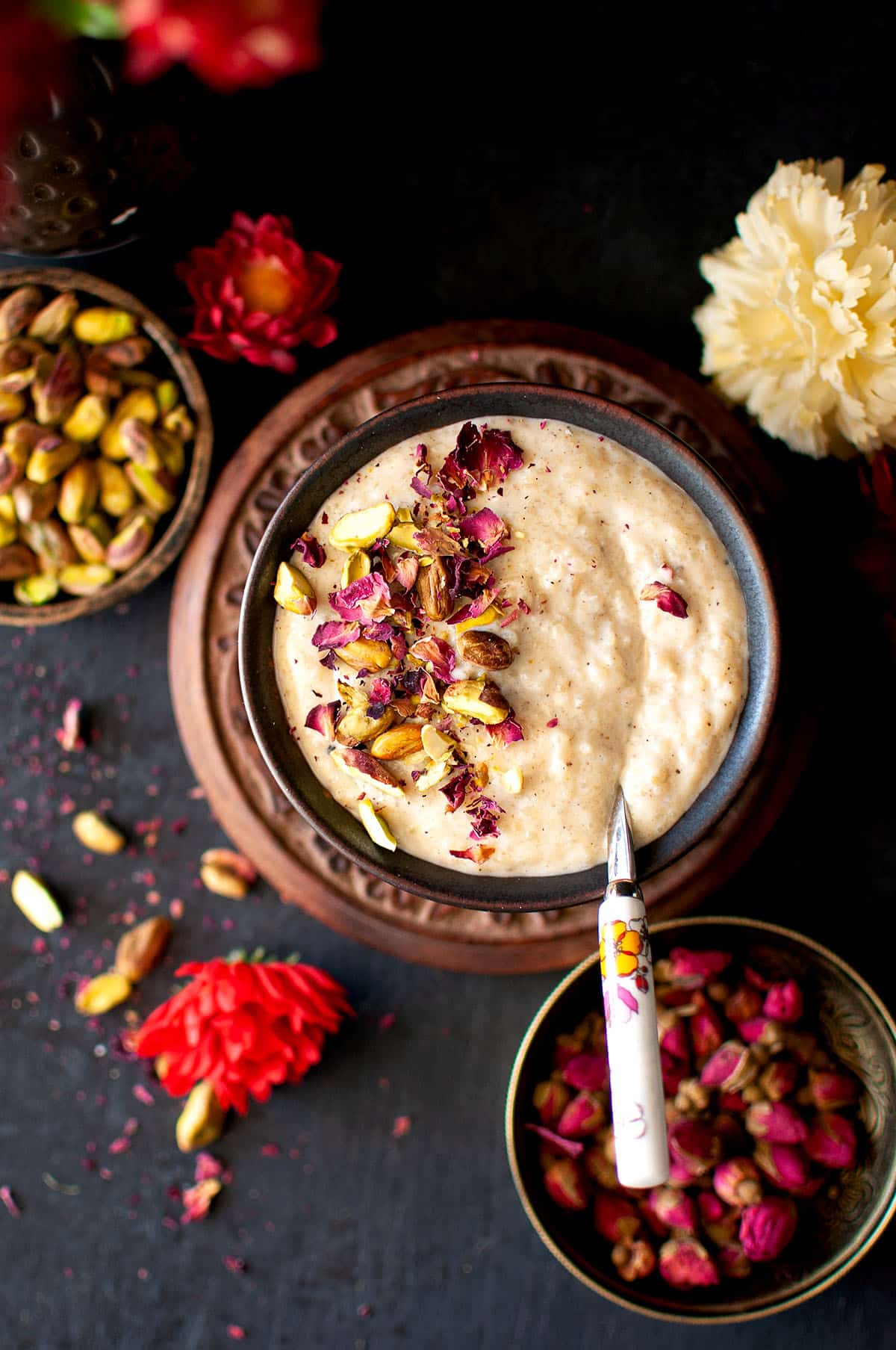 Black bowl with creamy rice pudding topped with rose petals and nuts.