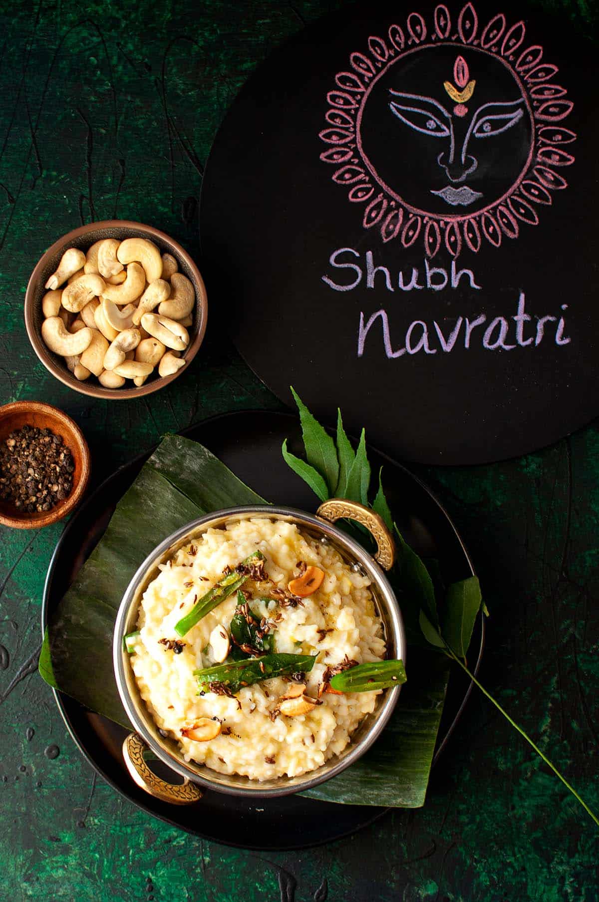 Steel bowl with Ven pongal and little bowls of cashews and peppercorns.