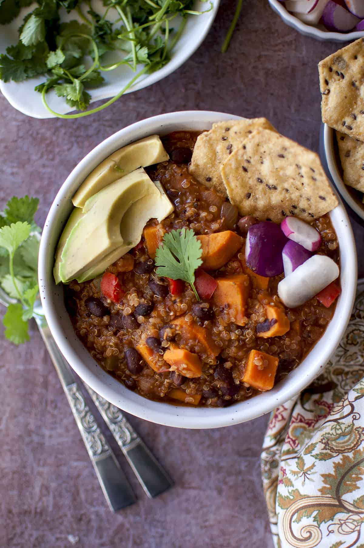 White bowl with the sweet potato quinoa chili topped with avocado, radish, cilantro and chips