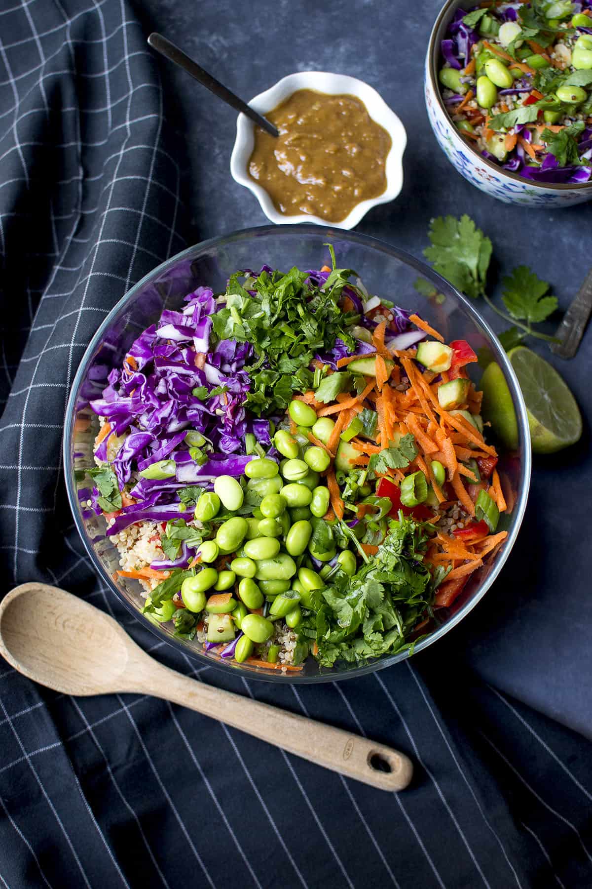 Top view of a glass bowl with veggies and quinoa and a small white bowl with dressing