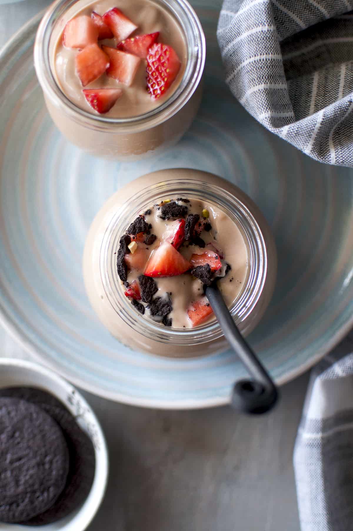 Chocolate custard topped with chopped berries, crushed cookies and nuts in a glass bottle with a spoon inside