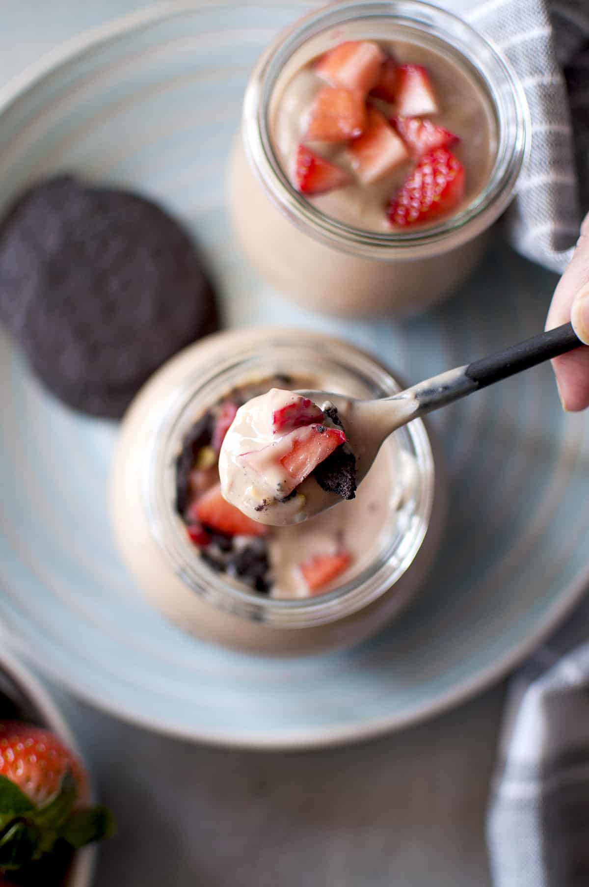 Hand met een lepel met chocoladepudding en aardbeien