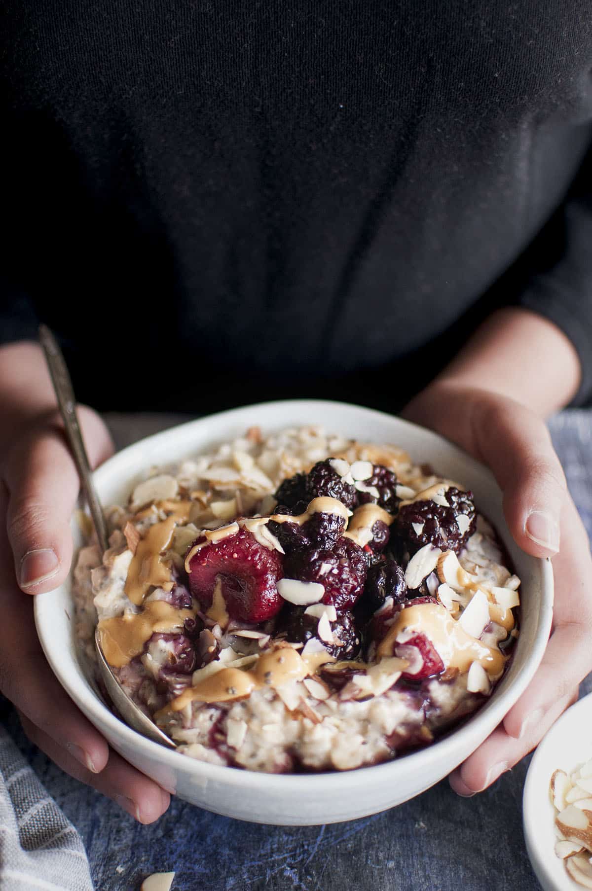 Hands holding gray bowl with oatmeal porridge with topping.