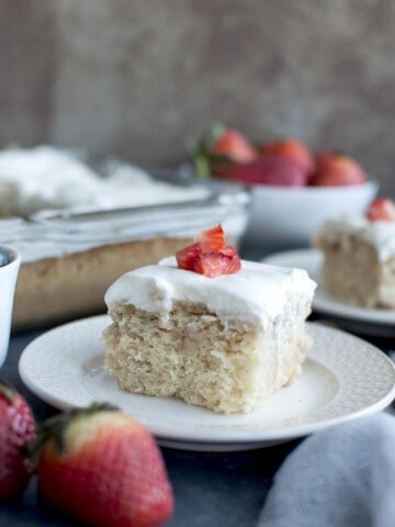 White plate with a slice of Vegan Tres Lech Cake topped with whipped cream and chopped berries