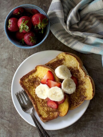 White plate with 2 slices of eggless French toast topped with chopped fruit