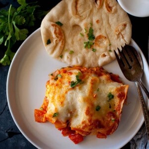 White plate with a slice of lasagna and naan