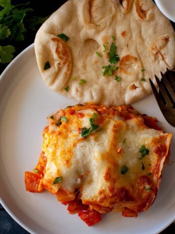 White plate with a slice of lasagna and naan