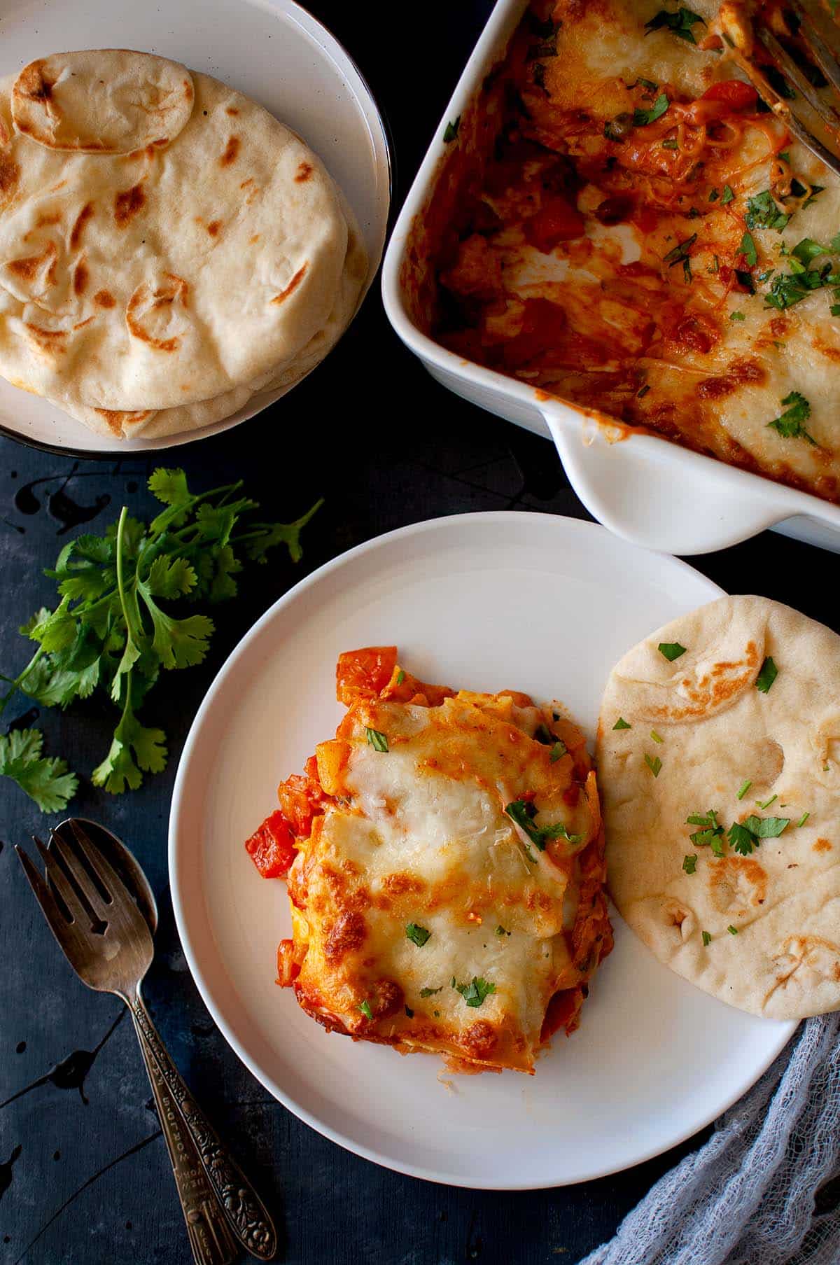 White plate with a slice of paneer lasagna and naan