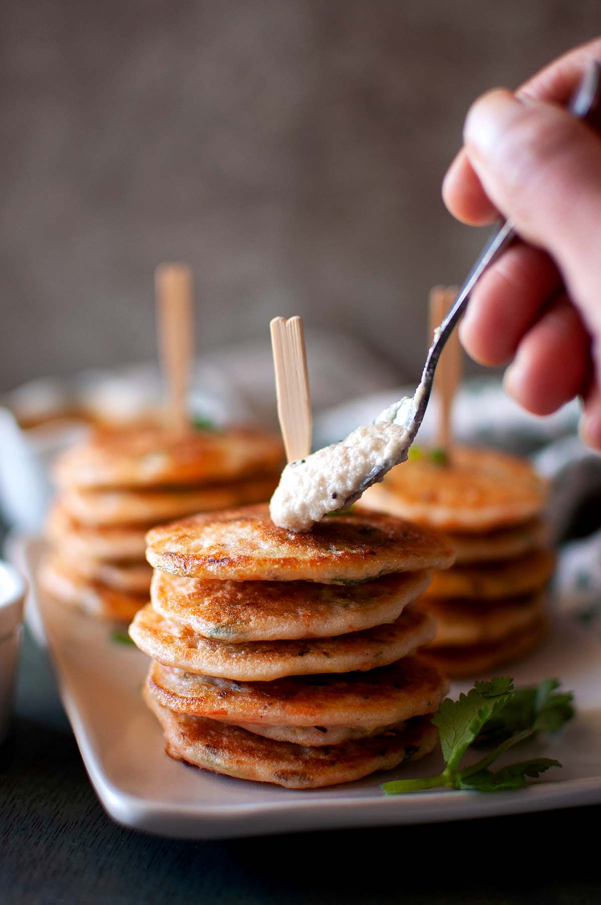 Hand putting a dollop of chutney on top of uttappam.